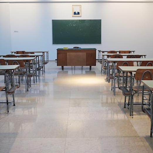 Photo of a school classroom with tables, chairs, and a chalkboard.